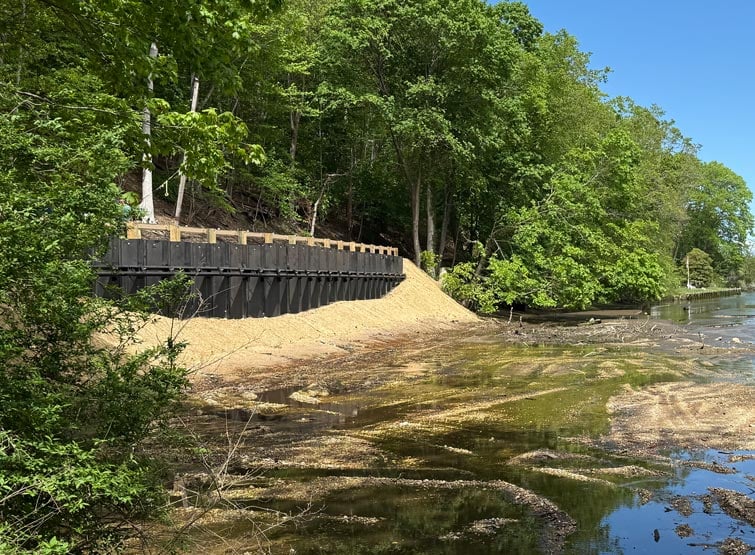 Reconstructed road next to water and sand with trees around.