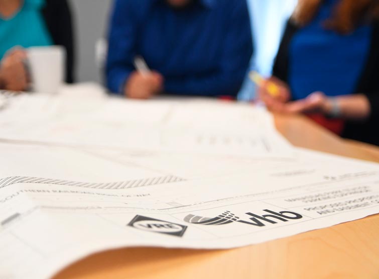 Sheet of VHB paper on desk with people’s hands in background.