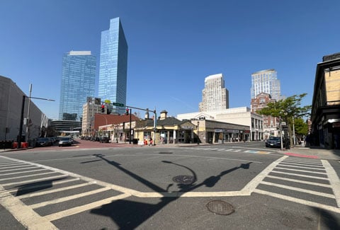 Street intersection featuring crosswalks, traffic lights, and a mix of modern skyscrapers and older low-rise buildings under a clear blue sky. 