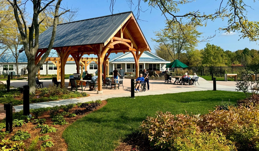 Residents gather under a timber pavilion beside a landscaped patio at a nursing and rehabilitation center. 