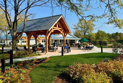 Residents gather under a timber pavilion beside a landscaped patio at a nursing and rehabilitation center. 