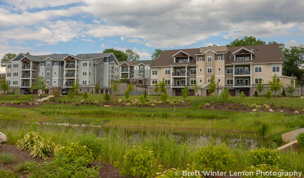 Two 4-story senior living buildings with stormwater ponds in the foreground on a partially cloudy day. 