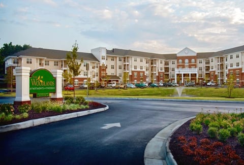 A 4-story senior living facility with a green lawn, fountain and landscaped roadways in the foreground. 