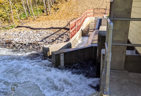 A small dam channeling water through a concrete spillway with turbulent flow.