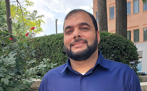 Adeel Mysorewala stands outdoors smiling at the camera in a navy-blue shirt.