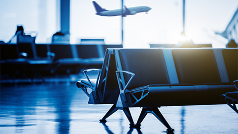 Empty chairs in the departure hall at airport , with an airplane taking off at sunset. blue toned.