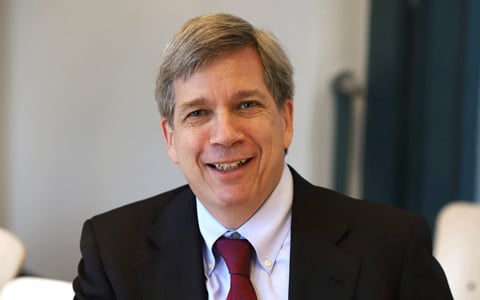 Alan Summerville smiles at the camera in black coat and red tie.