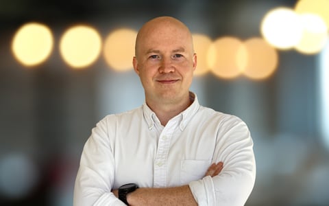 Andrew wearing a white shirt standing with his arms folded.