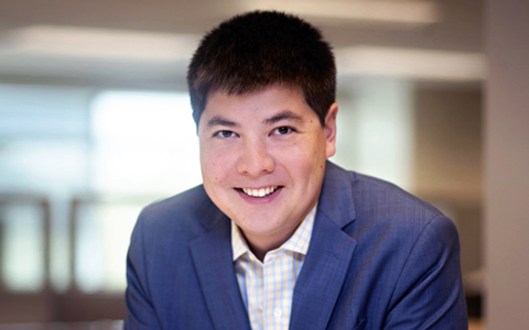 Andrew Nee leaning on a table at VHB while wearing a blue blazer.