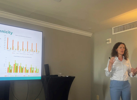 Woman presenting with a projection screen behind her.
