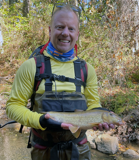 Jeff stands in a stream holding a pale yellow fish.