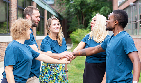 Five VHB employees standing in a circle outside cheering with their hands together in the center