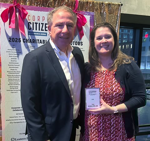 Two individuals at a corporate event smiling and holding a Corporate Citizenship Award.