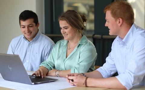 Drew Dommel, Aimee Barnes, and Matt Bruno gather together around a laptop in office.