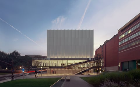 A dimly lit large building with a blue and purple sunset behind it and students walking through the site.