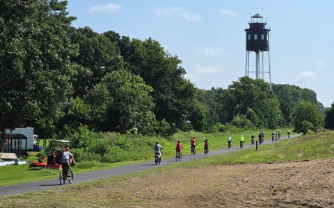 Bicycle riders on a rural bike path with a water tower in sight.