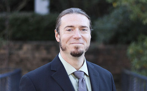 David Cooper smiles at the camera wearing a suit and tie.