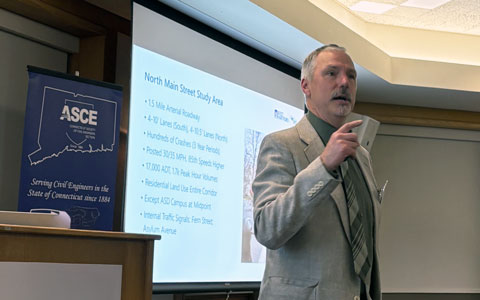 A person is speaking at a podium in a conference room. Behind them, a presentation slide displays text titled "North Main Street Study Area."