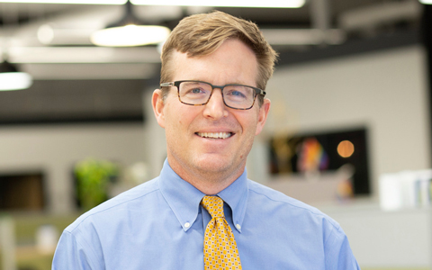 Man with glasses and tie standing in an office.