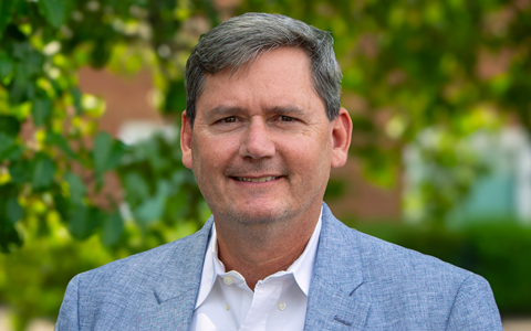 Head shot of Dan Wintermeyer in a light blue suit with a white shirt outdoors with trees in the background.