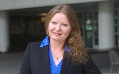 Danielle wears a blue shirt and black jacket in a professional setting outside a building