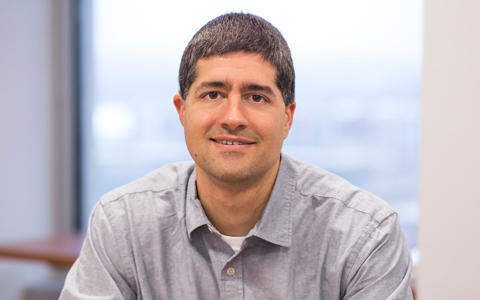 David Bost smiles at the camera in a gray button up shirt.