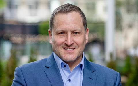 David Geller smiling in blue suit and tie. 