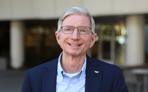 David is smiling while standing outside an office building.