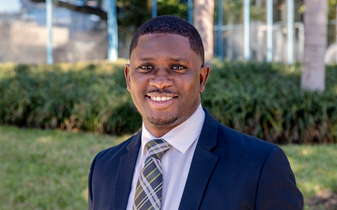 Demond Hazley wears a business suit and tie while standing outside an office building