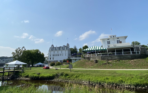 View of a serene river landscape with distinctive white buildings and green trees under a clear blue sky.