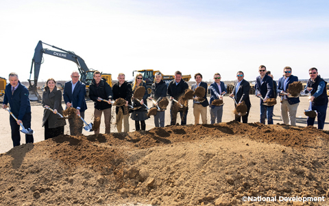 Men and women stand with shovels in their hands during a groundbreaking ceremony.