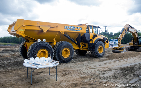 A groundbreaking ceremony with hardhats, shovels, and a dump truck.