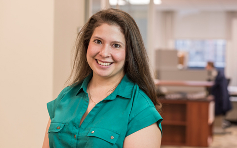 Elizabeth Jule wearing a teal shirt with the office in the background.