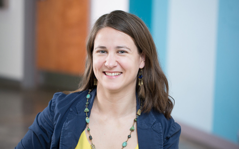 A woman with long brown hair wearing a blue jacket and turquoise necklace