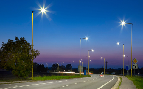 Street lights light up the evening sky at a turn on suburban road lined by trees