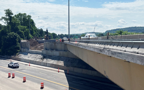 View of a highway under construction with traffic cones lining the lane barriers, under a clear sky.