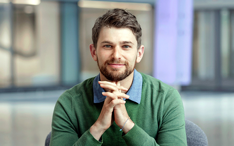 Image 1: Federico Tallis sitting in a chair wearing a green sweater.