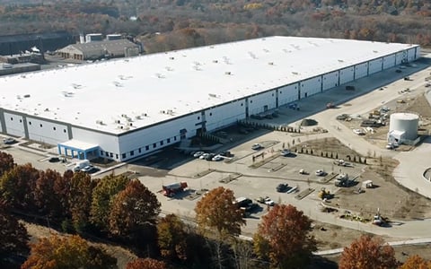 White industrial building with parking surrounded by trees.