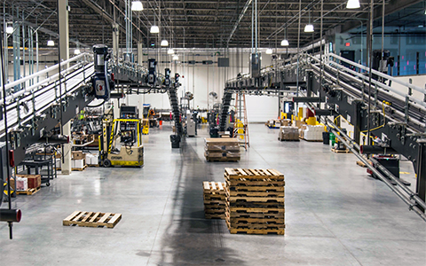 Pallets are stacked and automated machinery is shown centered inside a large industrial distribution warehouse
