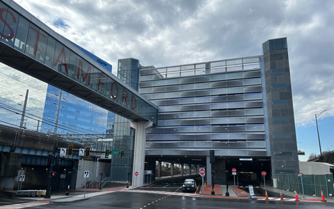A view of Stamford train station with a partly cloudy sky overhead. The entrance to a multi-level parking structure is on the right.
