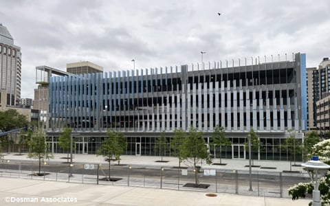 A modern multi-story parking garage with a sleek, blue and gray exterior is seen on a cloudy day.