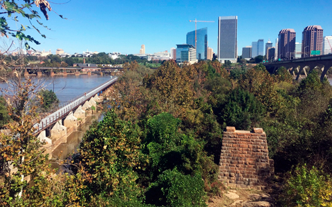 Pedestrian bridge across the James River with the skyline in the background.