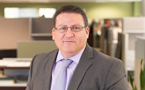 A business headshot of a man wearing a suit and tie in an office setting