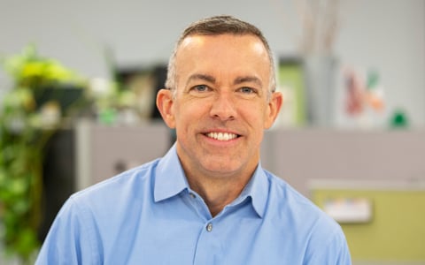 Joe Wanat smiles at the camera in a blue button-down dress shirt.