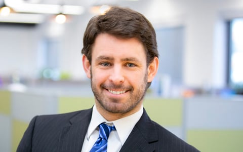 Ken Donald smiles in the office, wearing a blue striped tie and dark suit.