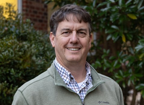 Kirby Marshall smiling in front of magnolia trees and a tan quarter zip.