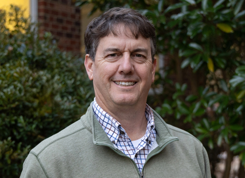 Kirby Marshall smiling in front of magnolia trees and a tan quarter zip.