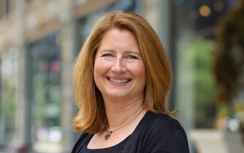 Lee Farmer in a black dress on a city sidewalk in the daytime with buildings in the background.