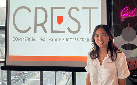 CREST Intern, Lily Liu stands in front of the CREST sign wearing a white top and maroon skirt