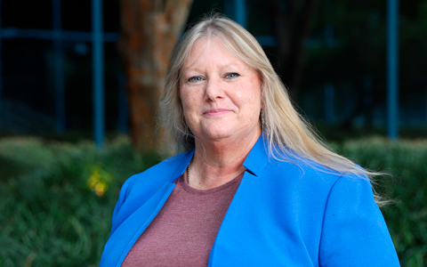 Liz Stutts stands outside an office building wearing a blue jacket